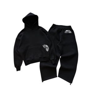 Puede incluir: Conjunto de sudadera con capucha y pantal&oacute;n de ch&aacute;ndal negros. La sudadera tiene un bolsillo delantero y una capucha. Ambas piezas tienen un parche circular con texto y un dise&ntilde;o. El pantal&oacute;n de ch&aacute;ndal tiene un bolsillo trasero.