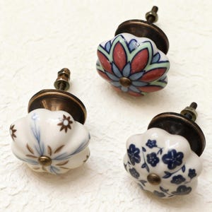 May include: Three decorative ceramic cabinet knobs with floral designs. One knob features a red, blue, and green floral pattern. Another has a blue and brown floral design. The third knob has a blue floral pattern.