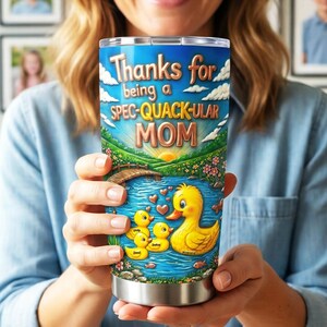 May include: Stainless steel tumbler with a whimsical design. The tumbler features a blue sky background with the words "Thanks for being a SPEC-QUACK-ULAR MOM." A pond scene with a mother duck and ducklings is also depicted.