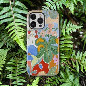 May include: A colorful phone case featuring a floral design with strawberries, blue flowers, and large green leaves. The case has a beige border and a glossy finish, with a camera cutout for a smartphone.