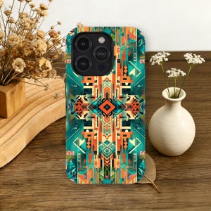 May include: A phone case with a geometric pattern in teal, orange, and black. The design features a central diamond shape and vertical lines. The case has a camera cutout and is displayed on a wooden surface.