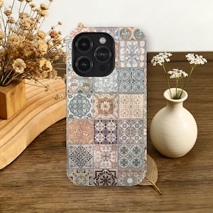 May include: A phone case with a mosaic tile pattern in beige, blue, and brown. The case has a camera cutout and is displayed on a wooden surface. The design is reminiscent of traditional tiles.