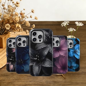May include: A collection of five phone cases with floral designs. The cases feature various colors, including black and white, blue, and purple, with a glossy finish. The cases are arranged on a wooden surface, with dried flowers in the background.