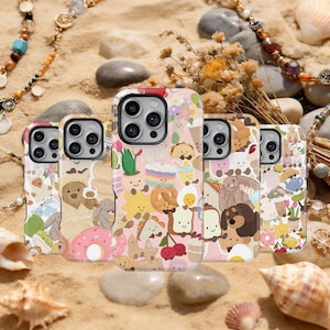 Puede incluir: Una colección de fundas para teléfonos con diseños coloridos de dibujos animados de comida y animales. Las fundas presentan imágenes de donuts, tacos, pan y animales sonrientes. Las fundas se exhiben sobre una superficie arenosa con conchas marinas y joyas.