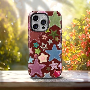 May include: A burgundy phone case adorned with various colorful star shapes. The stars are in shades of blue, green, pink, and silver, with stitched detailing. The case has a glossy finish and a camera cutout.