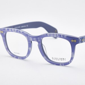 May include: Blue eyeglasses with a patterned design on the frames and arms. The glasses have a square shape and clear lenses. The brand name "GIULIANI OCCHIALI" is visible on the frame.