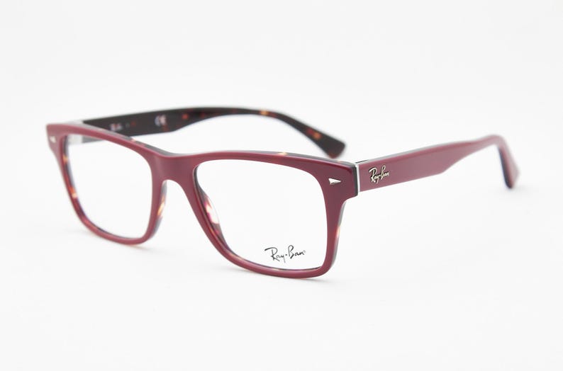 May include: Burgundy-colored eyeglasses with a rectangular frame. The temples and inner frame feature a tortoiseshell pattern. The Ray-Ban logo is visible on the temple and lens. The glasses are set against a white background.