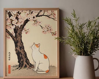 May include: A framed print featuring a white cat with orange markings, sitting under a cherry blossom tree. The artwork has a vintage aesthetic, with Japanese text and a red seal. The print is displayed on a wooden surface.
