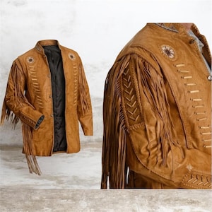 May include: A tan leather jacket featuring long fringe detailing on the sleeves and chest. The jacket includes a black interior lining, a stand-up collar, and decorative braided leather accents along the shoulders and front panels.