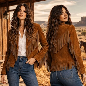 Puede incluir: Una chaqueta de ante marrón con largos flecos en el pecho, la espalda y las mangas. La chaqueta se lleva sobre una camisa blanca abotonada y vaqueros azules, mostrando un cuello estructurado y mangas largas con adornos de flecos.