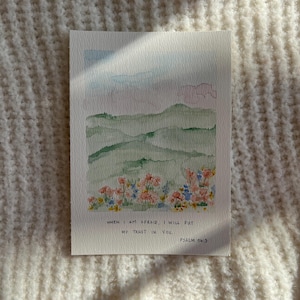 Può includere: Dipinto ad acquerello di un paesaggio con colline verdi, un cielo blu e rosa e fiori colorati. Il testo recita: "WHEN I AM AFRAID, I WILL PUT MY TRUST IN YOU. PSALM 56:3."