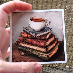 May include: A watercolor illustration of a white teacup with a brown handle, filled with tea, sitting on top of a stack of five vintage books. The books are stacked on a wooden table.