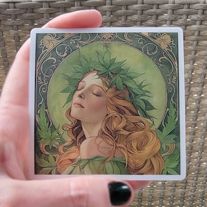 May include: A square sticker with a vintage illustration of a woman with her eyes closed. She is wearing a crown of green leaves and has long, flowing red hair. The background is a green and gold design.