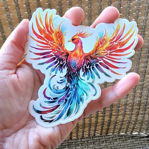 May include: A colorful phoenix sticker with red, orange, yellow, blue, and purple wings. The phoenix is in flight with its wings spread wide.