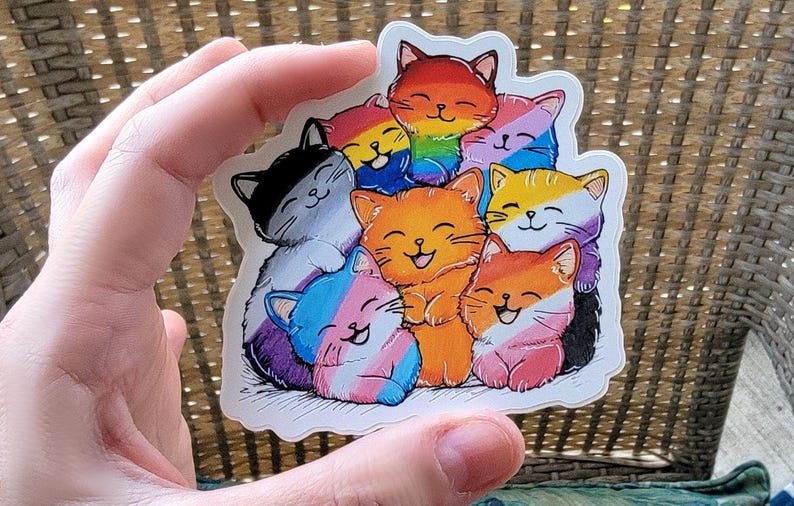 May include: A sticker featuring a group of seven cartoon cats, each with a different color and pattern, representing the LGBTQ+ pride flag. The cats are stacked on top of each other, with the largest cat at the bottom and the smallest cat at the top. The cats are all smiling and have happy expressions.