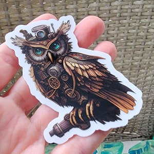 May include: A sticker featuring a detailed illustration of a steampunk owl. The owl has intricate mechanical details, including gears, goggles, and a top hat. The color palette includes browns, golds, and teal, creating a vintage aesthetic.