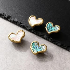 Peut inclure: Quatre boutons de meuble en forme de cœur. Deux boutons ont une incrustation de nacre blanche et deux ont une incrustation d'ormeau bleu-vert. Les boutons ont un cadre en métal doré avec de petits rivets décoratifs sur le bord.