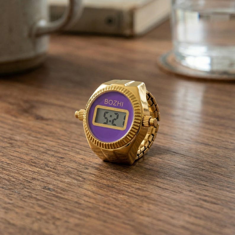 May include: A gold-colored digital ring watch with a purple face displaying the time 5:21. The watch has the brand name "BOZHI" above the time. The ring band is made of small, connected gold links.