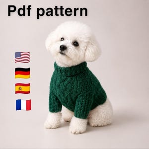 May include: A white Bichon Frise dog wearing a dark green cable-knit sweater with a ribbed turtleneck and cuffs. The text 'Pdf pattern' is visible at the top left, accompanied by four small flag icons representing the United States, Germany, Spain, and France.