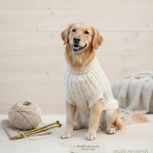 May include: A golden retriever wearing a cream-colored cable knit sweater. Beside the dog sits a ball of yarn with two knitting needles. A small tag on the floor displays the text "mallowmesh Handmade" and the word "mallowmesh" is printed nearby.