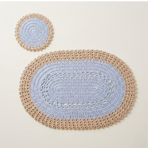 May include: A light blue and beige crochet oval rug and matching coaster set. The rug features a light blue centre with a beige border. The coaster is round with a light blue centre and beige border. The set is handmade.