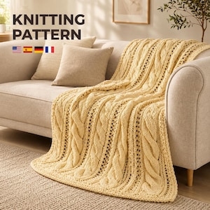 May include: A pale yellow knitted throw blanket featuring a prominent vertical cable stitch pattern and openwork detailing. The text KNITTING PATTERN is displayed in the upper left corner, accompanied by small flag icons for the US, Spain, Germany, and France.