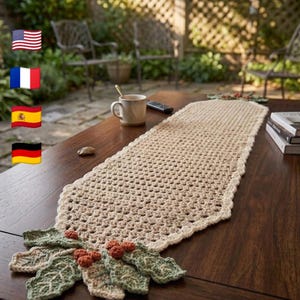May include: A cream-colored, crocheted table runner with a scalloped edge, adorned with crocheted holly leaves and berries. The runner is displayed on a dark wooden table, creating a cozy, handcrafted aesthetic. The runner is approximately 60 inches long.