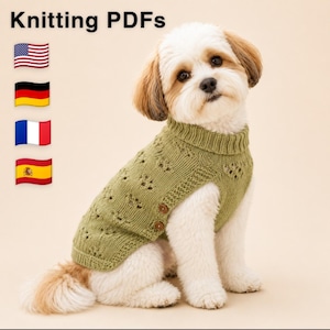 May include: A small dog with white and brown fur wearing a sage green knitted jumper with a ribbed collar, eyelet patterns, and two brown buttons on the side. The text Knitting PDFs is visible at the top with flags for the US, Germany, France, and Spain.