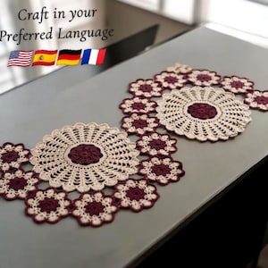 May include: Two handmade crochet doilies in a floral design. The center of each doily is a deep burgundy color, surrounded by a cream-colored crochet pattern. The doilies are surrounded by smaller burgundy and cream-colored flower-shaped crochet pieces. The text "Craft in your Preferred Language" is at the top.