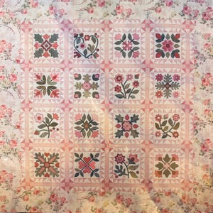 May include: A square quilt featuring a grid of sixteen blocks, each displaying unique floral and heart-shaped appliqué designs in shades of pink, green, and muted red. The quilt is framed by a wide border with a repeating pink rose pattern.