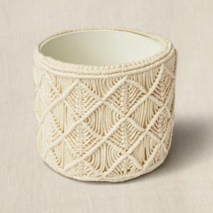 Op de afbeelding: Een cilindervormige, crèmekleurige macrame-mand met een ruitpatroon. De mand heeft een gladde, lichtgeleurde binnenkant en is geschikt voor kleine items of planten. De geweven textuur geeft een ambachtelijke, bohemien uitstraling.