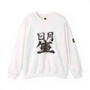 以下が含まれることがあります： 前面に黒い日本の書道デザインが施された白いクルーネックのスウェットシャツ。デザインは3つの文字と渦巻く渦を特徴としています。小さなエンブレムが左袖にあります。