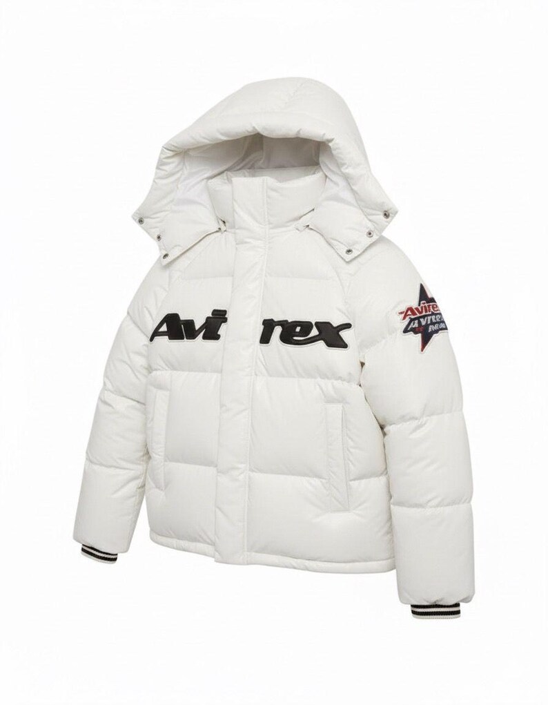Może przedstawiać: Biała kurtka puchowa z kapturem. Kurtka ma czarny napis "Avi rex" na piersi i naszywkę na rękawie. Mankiety mają czarno-białe paski.