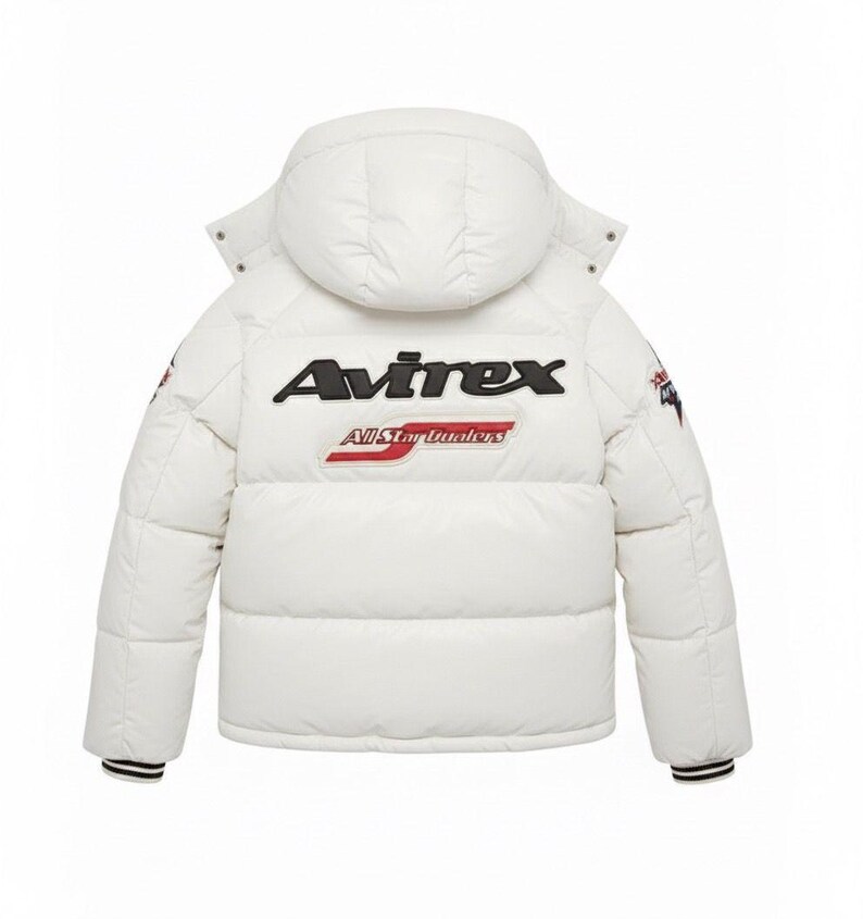 Może przedstawiać: Biała kurtka puchowa z kapturem, z nazwą marki "Avirex" w kolorze czarnym i napisem "All Star Dealers" w kolorze czerwono-białym. Kurtka ma czarno-białe paski na mankietach.