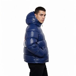 K&ouml;nnte beinhalten: Gl&auml;nzende, marineblaue Pufferjacke mit Kapuze. Die Jacke hat einen wei&szlig;en Streifen mit roten Akzenten auf der linken Schulter. Das Model tr&auml;gt eine schwarze Hose. Die Jacke hat einen Rei&szlig;verschluss und Taschen.