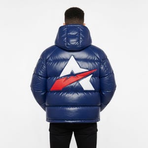 K&ouml;nnte beinhalten: Eine marineblaue Daunenjacke mit einem gro&szlig;en wei&szlig;en und roten Logo auf dem R&uuml;cken. Die Jacke hat eine Kapuze und eine gl&auml;nzende, gesteppte Textur. Die Person auf dem Bild tr&auml;gt eine schwarze Hose.