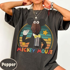 May include: Dark gray t-shirt featuring a cartoon Mickey Mouse character in a tuxedo and yellow bow tie, set against a circular background with a retro color scheme. The words "MICKEY MOUSE" are printed below the image.