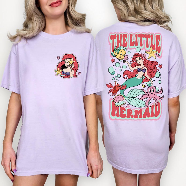 May include: Light purple t-shirt featuring a front pocket design of a mermaid holding a starfish. The back of the shirt has a larger graphic with the text "THE LITTLE MERMAID" and a mermaid with sea creatures.