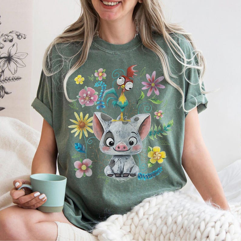 May include: Green t-shirt with a cartoon pig wearing a crown, alongside a rooster and flowers. The design is printed on a soft tee, suitable for everyday wear. The shirt has a relaxed fit and is a comfortable choice.