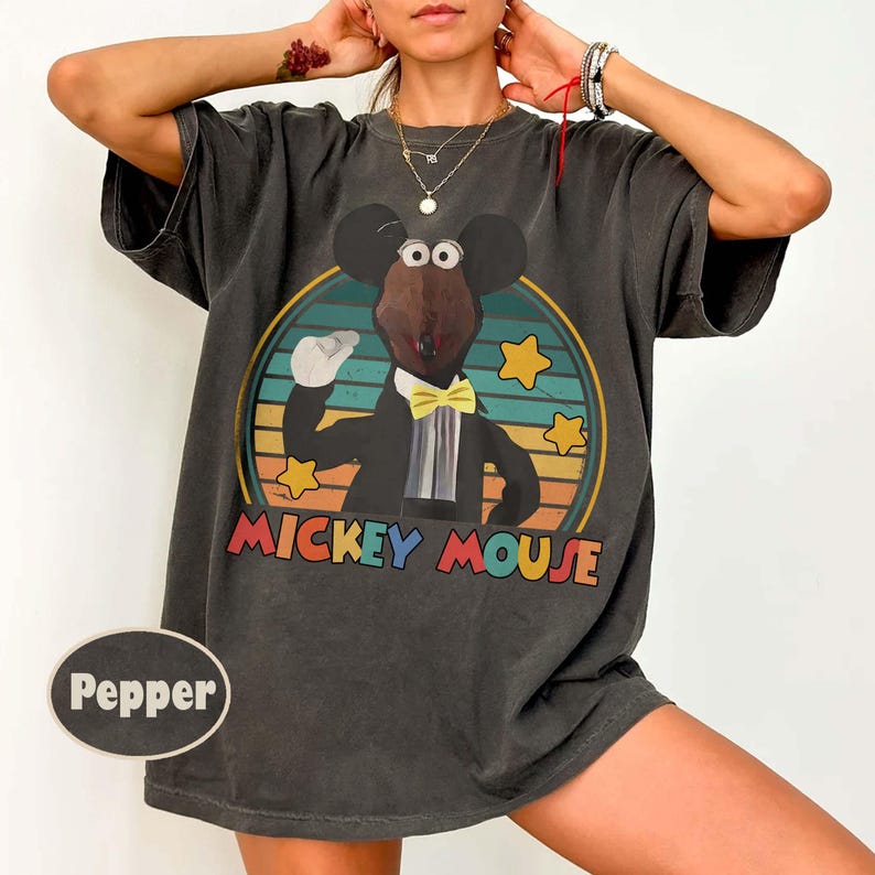 May include: Dark gray t-shirt featuring a cartoon Mickey Mouse character in a tuxedo and yellow bow tie, set against a circular background with a retro color scheme. The words "MICKEY MOUSE" are printed below the image.