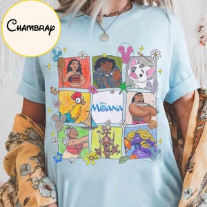 K&ouml;nnte beinhalten: Hellblaues T-Shirt mit einem farbenfrohen Grafikdesign von Charakteren aus dem Disney-Film Moana. Das Design zeigt Moana, Maui, Pua, Hei Hei und andere, mit dem Filmtitel in der Mitte. Das T-Shirt hat kurze &Auml;rmel.