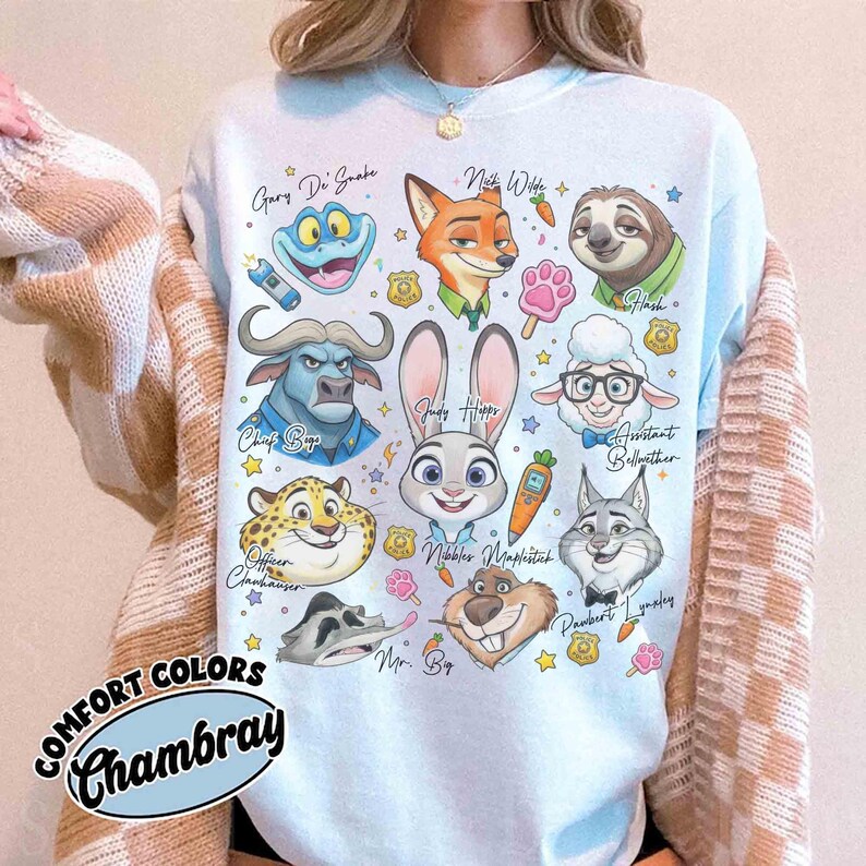 K&ouml;nnte beinhalten: Hellblaues Sweatshirt mit Zeichentrickfiguren aus Zootopia, darunter Judy Hopps, Nick Wilde und Flash. Das Shirt tr&auml;gt den Schriftzug "COMFORT COLORS Chambray" in Schreibschrift.