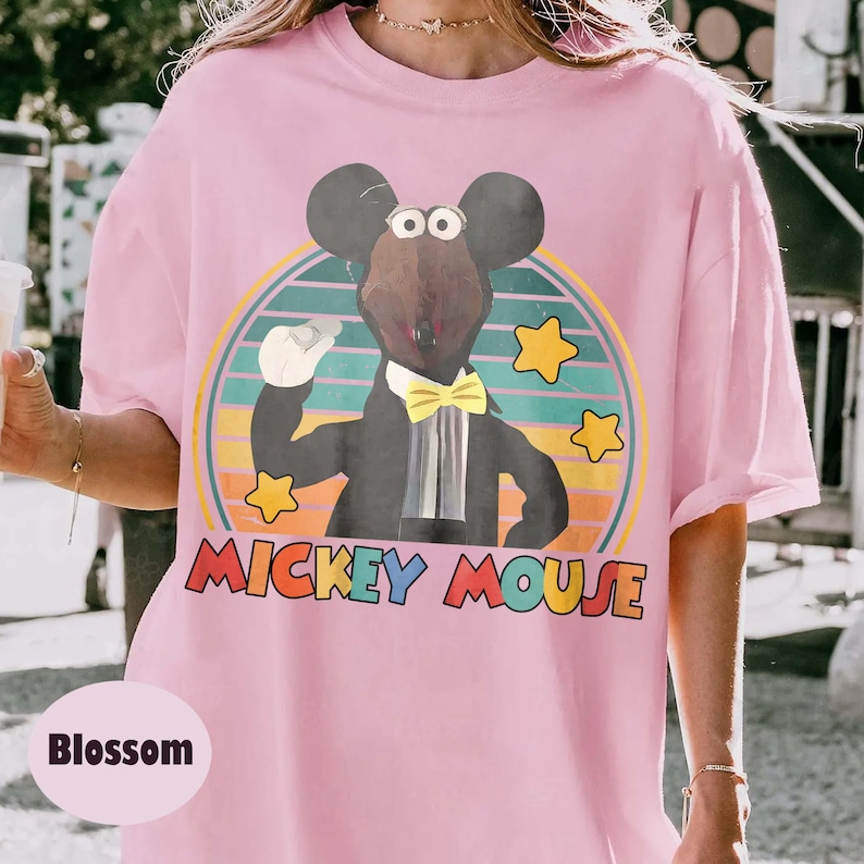 May include: Pink t-shirt with a graphic of Mickey Mouse in a tuxedo, yellow bow tie, and white gloves. The design includes a colorful retro circle and the text "Mickey Mouse". The shirt also has the word "Blossom".