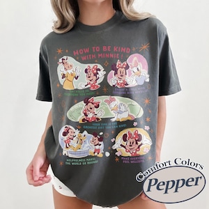 Peut inclure: T-shirt Comfort Colors gris fonc&eacute; avec un motif de Minnie Mouse et ses amis. Le t-shirt porte l'inscription "HOW TO BE KIND WITH MINNIE!" et d'autres phrases. Le t-shirt est de couleur poivre.