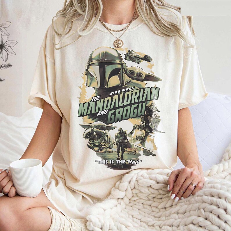 K&ouml;nnte beinhalten: Cremefarbenes T-Shirt mit einer Grafik aus der Star Wars-Serie "The Mandalorian and Grogu". Das Design zeigt den Helm des Mandalorianers, Grogu und den Satz "THIS IS THE WAY".
