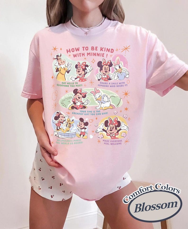 Peut inclure: T-shirt rose clair avec l'inscription "HOW TO BE KIND WITH MINNIE !" et des illustrations de Minnie Mouse et ses amis. Le t-shirt pr&eacute;sente &eacute;galement les mots "Comfort Colors" et "Blossom" dans un design circulaire.