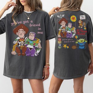 Op de afbeelding: Donkergrijs T-shirt met een afbeelding van Woody en Buzz Lightyear en de tekst "you've got a friend in me." De achterkant van het shirt heeft extra Toy Story graphics. Het T-shirt heeft een relaxte pasvorm.