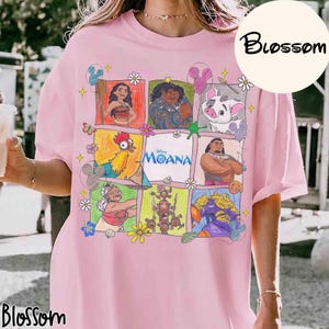 K&ouml;nnte beinhalten: Hellrosa T-Shirt mit einem farbenfrohen Grafikdesign von Charakteren aus dem Disney-Film Moana. Das Design zeigt Moana, Maui, Hei Hei, Pua und andere Charaktere, mit dem Wort "Moana" in der Mitte. Das Shirt hat das Wort "Blossom" in einem Kreis.