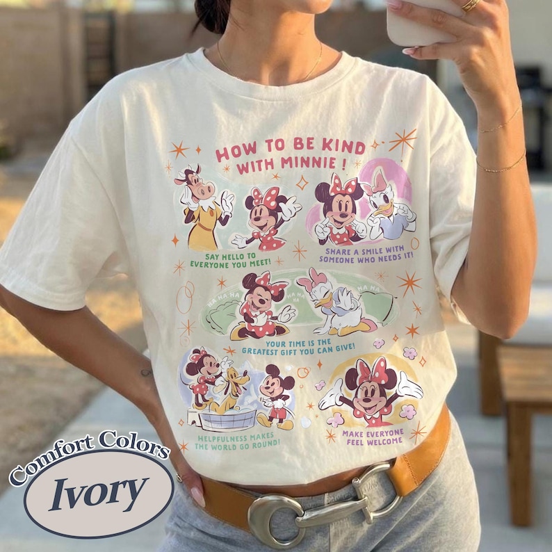 Peut inclure: T-shirt ivoire avec un motif de Minnie Mouse et ses amis. Le texte "HOW TO BE KIND WITH MINNIE!" est pr&eacute;sent, ainsi que des phrases comme "Dites bonjour &agrave; tout le monde !" et "Faites en sorte que tout le monde se sente bienvenu."