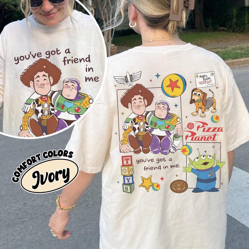 Op de afbeelding: Ivoor T-shirt met een afbeelding van Woody en Buzz Lightyear en de tekst "you've got a friend in me". De achterkant van het shirt toont andere Toy Story-personages en het Pizza Planet-logo.